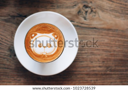 Panda latte art in cappuccino cup on wooden table. Pattern on coffee foam.