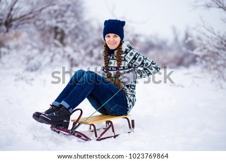 Cheerful young woman having fun on a sleigh in snowy weather