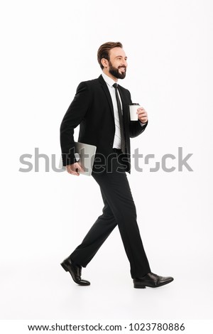 Photo of smiling young businessman walking isolated over white background. Looking aside holding laptop computer.