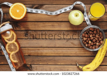 Healthy lifestyle; fitness bottle; fruits (oranges; apples and bananas); hazelnuts and peanuts; orange juice and measuring tape. Top view; the concept of free space for text
