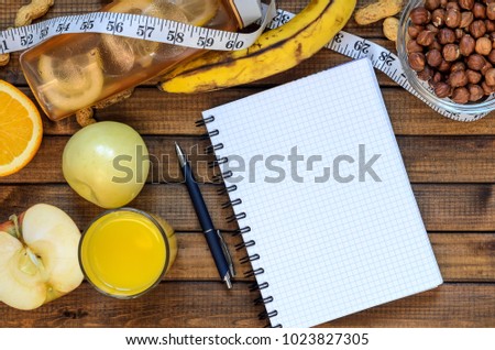 Healthy lifestyle; fitness bottle; fruits (oranges; apples and bananas); hazelnuts and peanuts; orange juice, a pen and a notebook and measuring tape. Top view; the concept of free space for text
