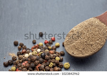 Closeup black pepper whole in wooden spoon on black stone table