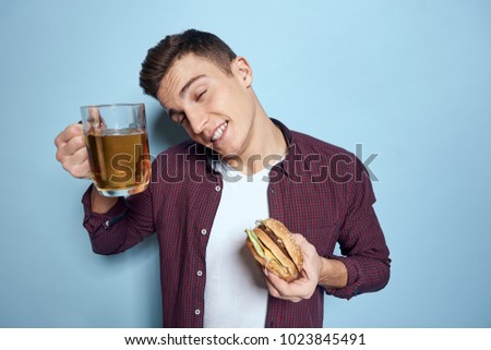   man smiling holding a burger, beer on a blue background                             