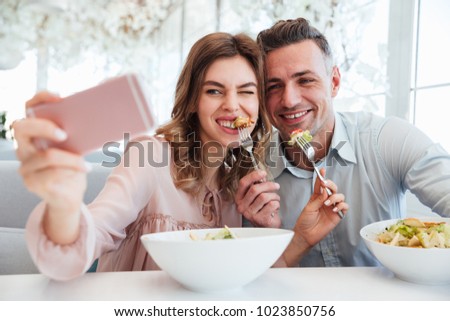 Portrait of a happy young couple taking a selfie while having lunch together at the cafe table indoors