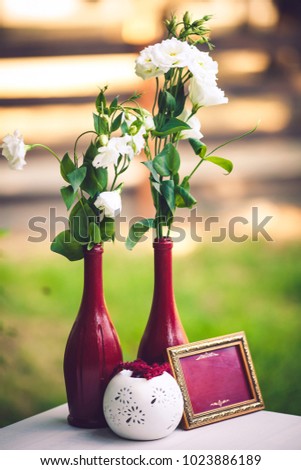 Decoration of the color of marsala on the wedding table: vases with flowers, bottles, photo frame. There is room for your text here.