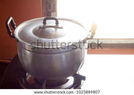 Stainless pot on gas stove with orange orange tiles by the window.