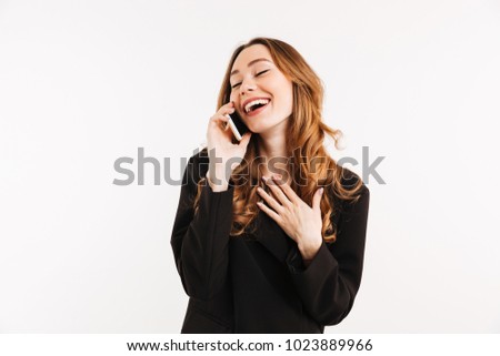 Smiling businesslike woman with long auburn hair in black talking on smartphone and having pleasant conversation, isolated over white background