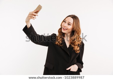 Image of sociable pretty woman in black jacket making selfie and smiling on her cell phone isolated over white background