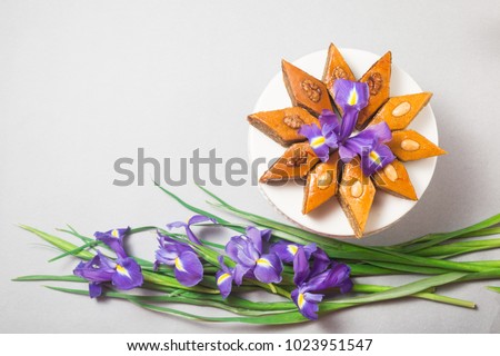 Plate of traditional Azerbaijan baked pastry dessert pakhlava baklava with walnuts and honey for Novruz holiday spring celebration with bouquet of purple flowers fleur de lis on light grey background 