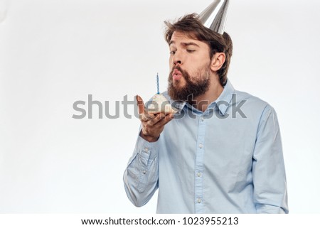  man blows a candle on a cake on a light background, birthday                              
