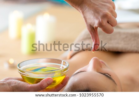 Macro close up of hand with oil drop above woman head in spa. Aromatic oil in glass bowl next to woman at Ayurveda massage. Royalty-Free Stock Photo #1023955570