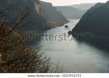 Danube between mountains/Narrow natural channel on the Danube river between the Carpathian mountains that constitutes the border between Romania and Serbia, where a barge is passing by a small church. Royalty-Free Stock Photo #1023956755
