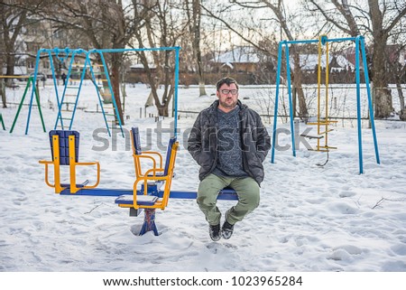 adult bearded man with glasses sitting on a swing, roundabout