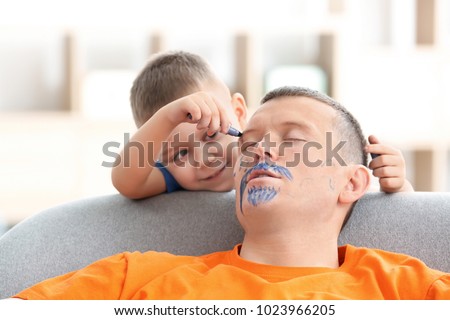 Little boy painting his father's face while he sleeping. April fool's day prank Royalty-Free Stock Photo #1023966205