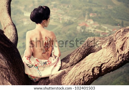 Asian style portrait of young woman sitting on the tree branch with snake tattoo on her back (original) Royalty-Free Stock Photo #102401503
