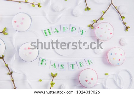 Top view holiday composition of Happy Easter lettering, branches with young shoots of greenery, decorated cupcakes, merengue sweets, bird figure on wooden background. Art concept. Selective focus