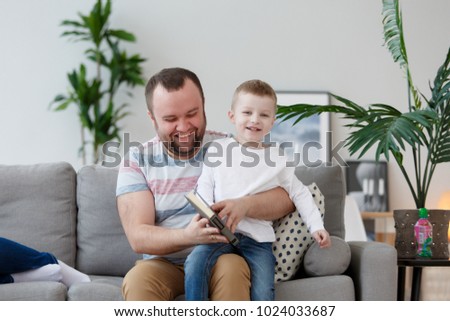 Photo of father and son reading book sitting on gray sofa