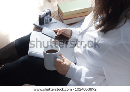 Woman sitting on a wooden floor white using a mobile connected to Internet. Self-employee worker making some paperwork. Empty copy space for Editor's text.