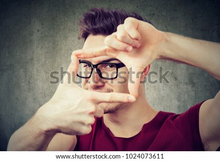 Young man making frame with hands creating shot and looking at camera. 