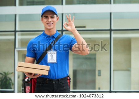 Portrait of handsome young delivery man with two pizza boxes showing ok sign