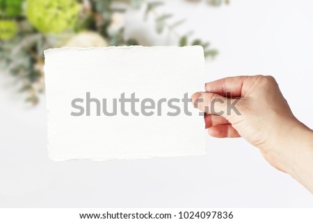 Styled stock photo. Feminine wedding, birthday greeting card mockup scene with woman's hand in holding blank paper card. Blurred floral background. Empty space. Picture for blog or social media.