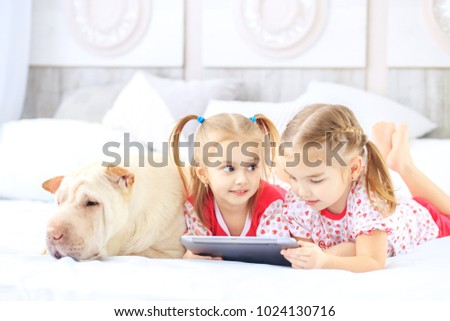 Two little children girls watching cartoons on the tablet. Dog. The concept of childhood, lifestyle, game.