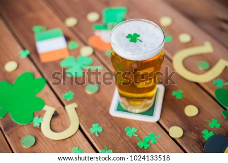 st patricks day, holidays and celebration concept - glass of draft beer, shamrock and gold coins on wooden table