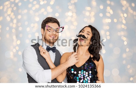 celebration, fun and holidays concept - happy couple posing with party props over festive lights background