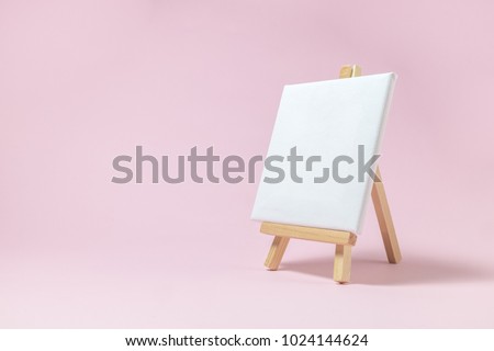Easel for artists and blank canvas miniature on pastel pink background. Art minimal concept.