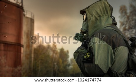Stalker soldier in gas mask and russian military hoodie jacket looking aside while walking in the danger radioactive zone with cisterns. Post apocalypse. Nuclear war. Royalty-Free Stock Photo #1024174774