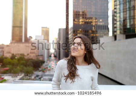 Beautiful young woman sitting on a bridge across the boulevard in urban scenery, downtown, at sunset, looking at side.