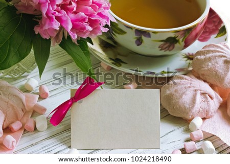 Peonies flowers with card marshmallow pink cup of tea on a white wooden background - stock image