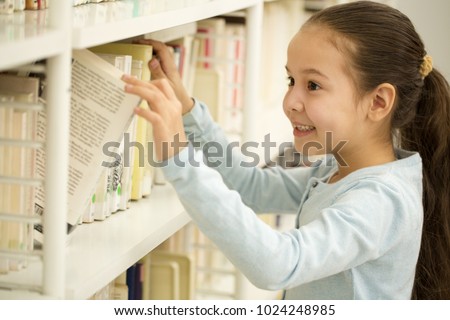 Happy cute little girl smiling joyfully choosing a book from the bookshelf at the library or bookstore copyspace school learning studying education childhood positivity lifestyle happiness.