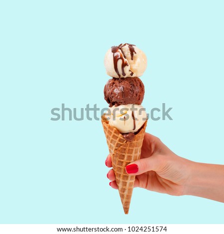 Chocolate and vanilla ice cream cone on faded pastel color background. Hand holding ice cream in wafer cup.