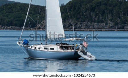 A blue and white sailboat is travelling in Frenchmans Bay off of the coast of Bar Harbor Maine on a beautifull summer afternoon.