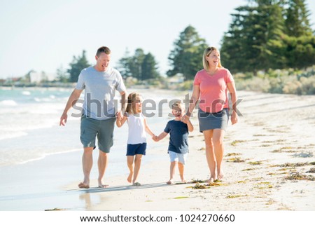 young happy and beautiful family mother father holding hand of son and daughter walking joyful on the beach enjoying Summer holidays in parents and siblings lifestyle concept