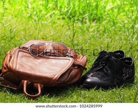 Travel accessories on green grass with blurry background, vacation concept, nature trip, brown leather bag, sunglasses and black shoes