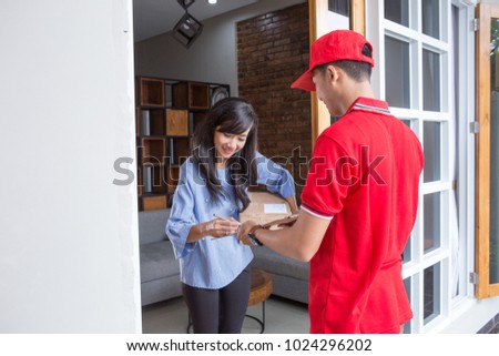 Smiling delivery man in red uniform delivering parcel box to recipient