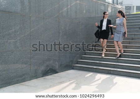 Two happy office lady finish their meetings and walk down stairs wirth fullfeeling .They speak to each other happily. on a front view . partnership concept .