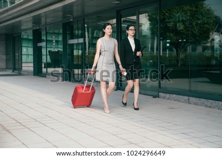 Asian modern office women walk on the hallway of the airport and one of them carrying a big red suitcase. They are going abroad. Royalty-Free Stock Photo #1024296649