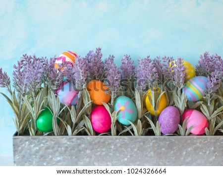 Colorful Easter Eggs Still Life Display with Lavender Flowers in Metal Planter against Blue Sky Background with room or space for copy, text, your words or design.  Horizontal with side view