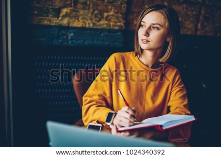 Thoughtful businesswoman pondering on strategy for design project making research in notebook.Contemplative student doing homework task solving problems and analyzing information in cafe interior Royalty-Free Stock Photo #1024340392