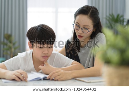 Asian woman helping asian boy doing homework on table at home.