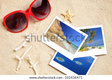 A sunglasses, few photos, starfish and corals on a sandy beach