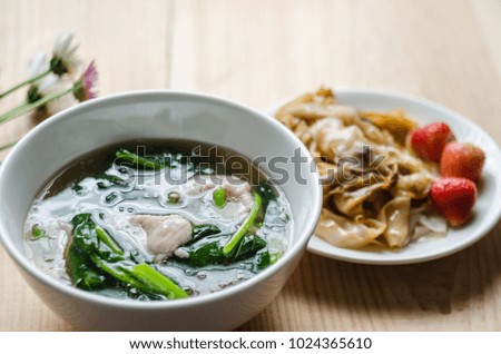 Fried noodle with pork and kale soaked in gravy in white bowl on a wooden table. Thai traditional food and popular menu. Still life image/ selective focus. 