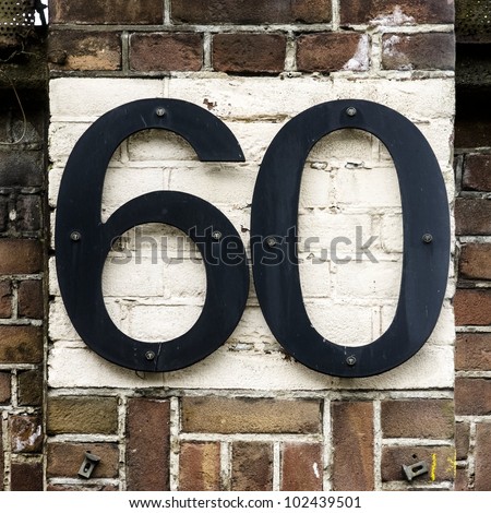 Rather large house number sixty attached with screws on a brick wall