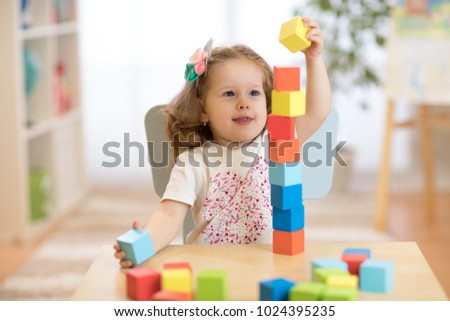 Cute child stacks building cubes sitting at table in nursery room Royalty-Free Stock Photo #1024395235