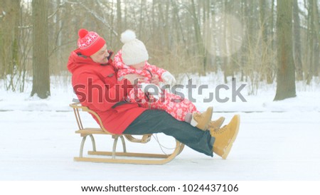 Happy little boy and his grandfather on the sledge in the winter park