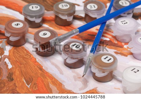 Painting on canvas by numbers. Numbered containers with paints and brushes lie on the canvas background.