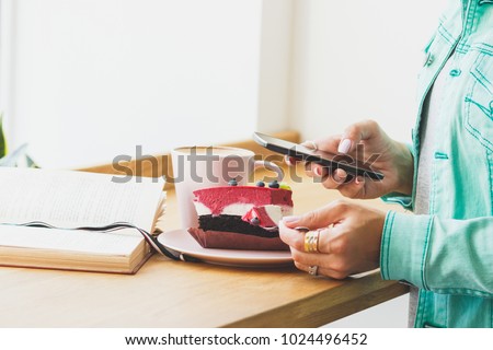 Woman with a cup of cappuccino and a piece of dessert on the spoon, soft focus background